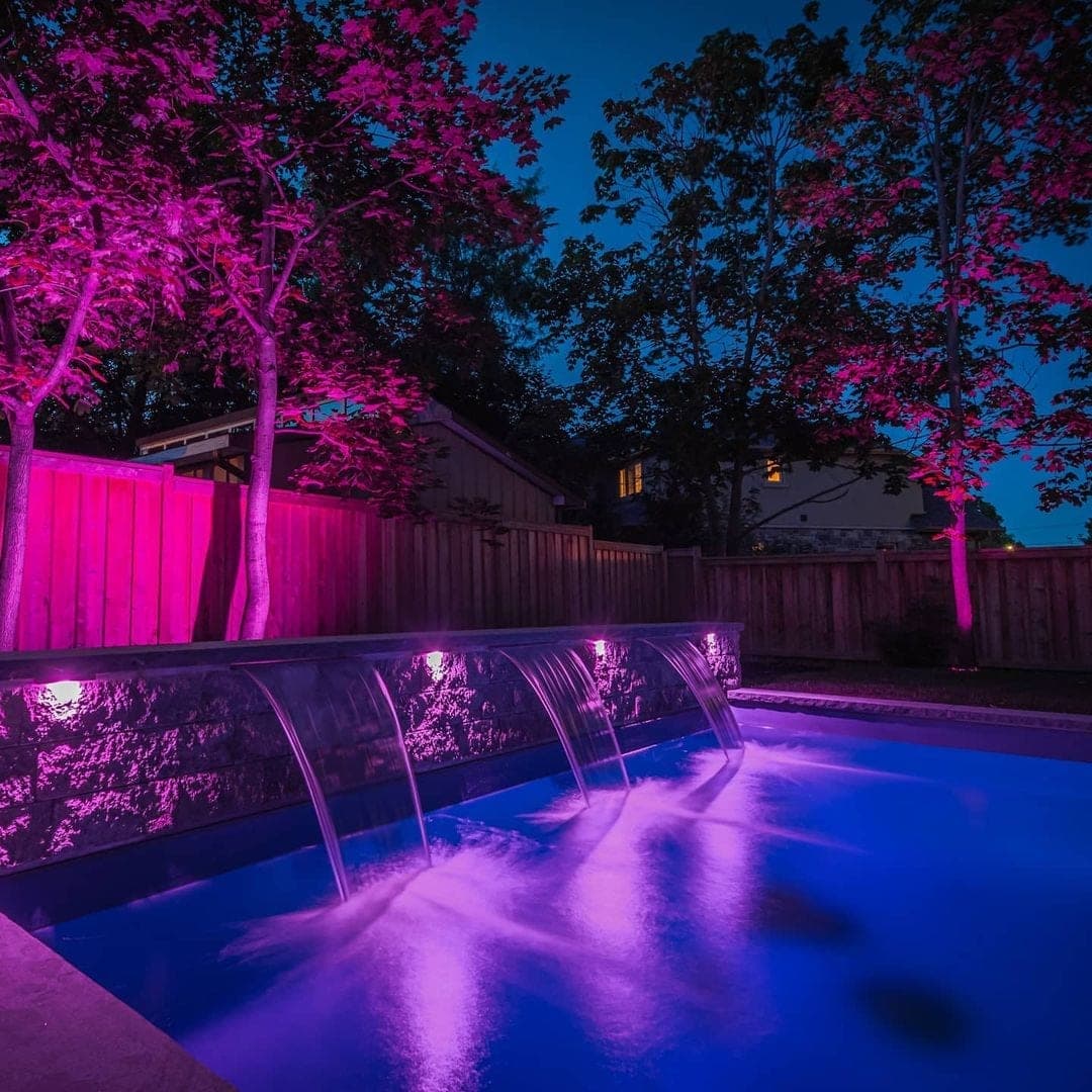 Pool waterfall with dramatic purple feature lighting at night